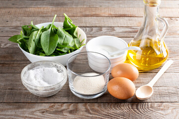 Set of raw ingredients for cooking healthy spinach pancakes on table (dough, psyllium, eggs, oil, sour cream and spinach leaves) Gluten free spinach pancakes recipe