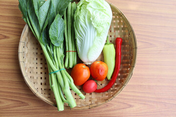 Vegetables in wicker basket isolated on wooden background closeup.