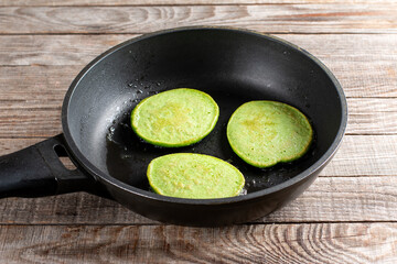 Homemade spinach pancakes on the frying pan on a wooden table. Healthy food, diet