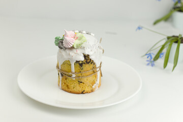 Orthodox Easter cake with white fondant and marshmallows tied with a rope on a plate with spring flowers in a pot, side view