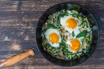 Shakshuka, fried eggs with green wild garlic leaves, onion, pepper and spices in cast iron pan, close up