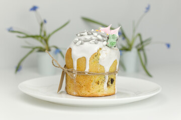 Orthodox Easter cake with white fondant and marshmallows tied with a rope on a plate with spring flowers in a pot side view