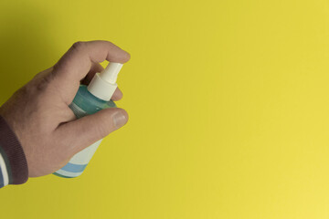 Hand pressing spray bottle on yellow background