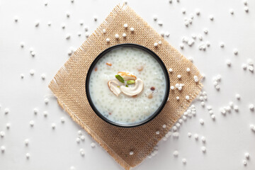 Close-up of Creamy Sabudana Kheer Garnished with dry fruits. Indian delicious dessert. Served in the black bowl. Top View on a white background and jute mat.