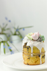 Orthodox Easter cake with white fondant and marshmallows tied with a rope on a plate with spring flowers in a pot