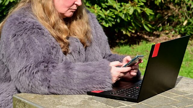 Frau in einer Kaninchenfell Jacke arbeitet im Garten mit einem Notebook im Homeoffice  