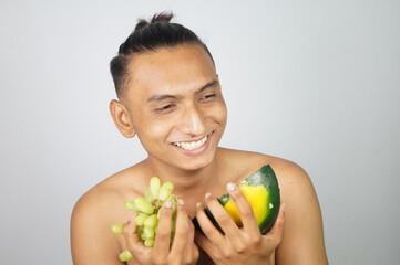 Naked South Asian man from India with grapes and slice of watermelon in hands on white background
