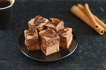 Pieces of chocolate cake lie in a saucer, next to cinnamon sticks and coffee