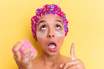 Young mixed race woman taking a bath holding a sponge with an under eye patches