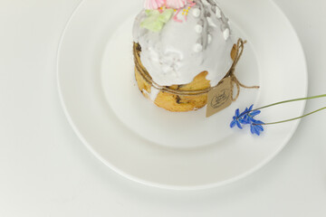 Orthodox Easter cake with white fondant tied with a rope with tag on a plate with spring flowers in a pot side view
