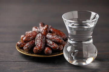 A glass of water and dry dates on saucer ready to eat for iftar time. Islamic religion and ramadan...
