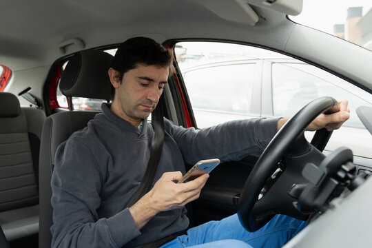 Young man driving car looking at cellphone on hand. Driver reckless behavior concept