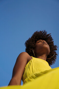 Low Angle Shot Beautiful Black Woman With Afro Wearing Yellow Dress Against Blue Sky