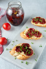 Sandwich with homemade mayonnaise, sun-dried tomatoes and micro greens, served on a board on a gray background