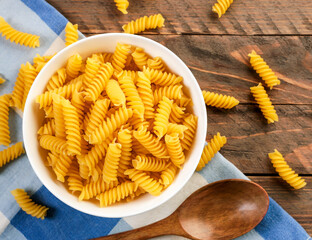 Raw spiral pasta in a plate on a wooden background. The view from top