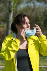 WOMAN RUNNER WITH YELLOW WINDBREAKER PUTTING ON HER FACE MASK