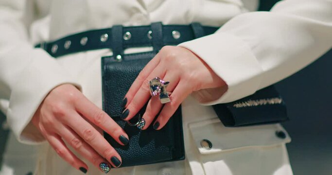 Slow motion stylish accessories business 4K commercial footage. Close up model in trendy white jacket with black manicure and metallic ring opening fashionable black belt with pockets and mini bags