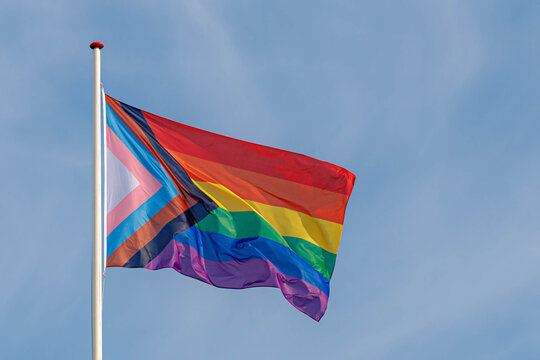 Progress pride flag (new design of rainbow flag) waving in the air with blue clear sky, Celebration of gay pride, The symbol of lesbian, gay, bisexual and transgender, LGBTQ community in Netherlands.