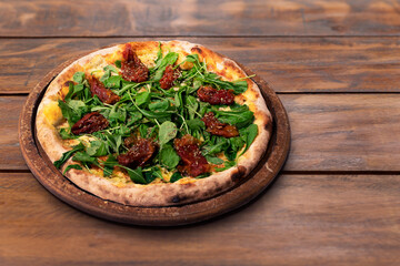 Arugula pizza with dried tomatoes on a wooden table.