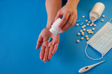 Medicine and healthcare concept. The woman removes the capsule from the container. Capsules, pills, medical mask on a blue background. Place for your text.