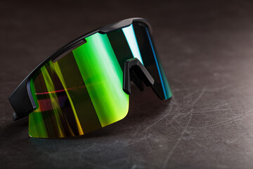 Sports glasses with a green mirrored lens on a black textured background.