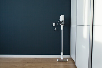 Modern cordless vacuum cleaner charges against a blue wall. Minimalistic interior.