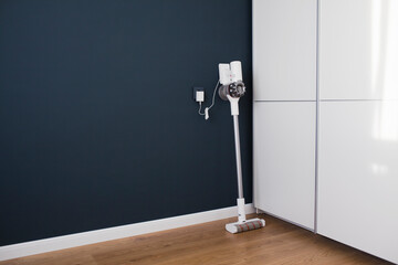 Modern cordless vacuum cleaner charges against a blue wall.