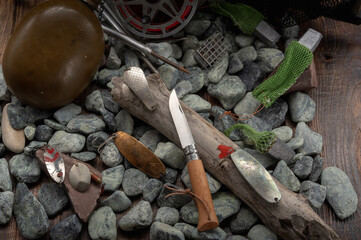 Fishing tackle and a knife on the stones. Pocket knife on wood.