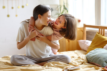 Young beautiful mom with happy little child embracing and expressing love while sitting together on the bed