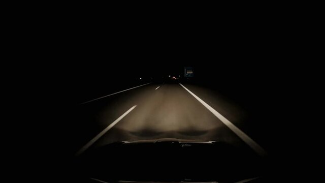 Driving in a pitch black night on a highway. View from the windshield, light cone with road markings