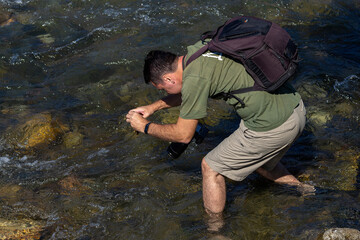 A young man, a naturalist photographer who takes photos and videos on a mountain river on a sunny summer day.
