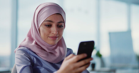 Excited arabic Muslim woman in hijab receiving good news on smartphone celebrating and clenching fists. Victory concept.