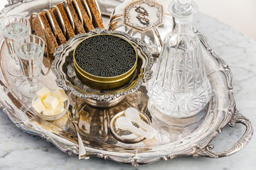 Black caviar on ice in silver bowl, Vodka and bread on white marble table