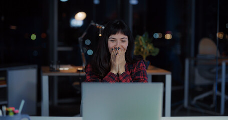 Cheerfull emotional young woman engaged in business working late at office reading news celebrating...
