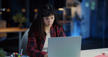 Young Emotional Caucasian Woman Executive Working Late at Office Communicating on Laptop Typing Messages on Social Media. Casual Lifestyle.
