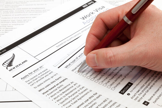 A man holding a ballpoint pen to fill a work visa application form to New Zealand.