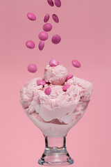 Pink ice cream in a cup with pink candies falling on it, shot in studio over a pink background