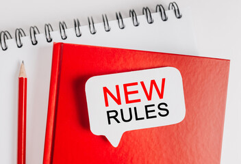 Text new rules a white sticker on red notepad with office stationery background. Flat lay on business, finance and development concept