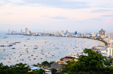 Fototapeta premium Panoramic view of the city and the bay with boats and yachts at sunset. Pattaya city and the sea at dusk, Thailand.