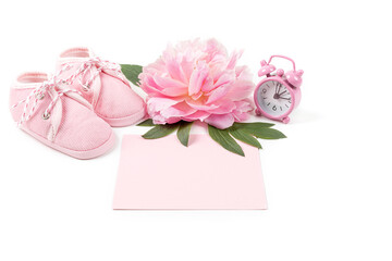 Pink baby girl shoes with peony flower, alarm clock and a blank card for message on a white background. Newborn greeting card or invitation. Copy space.