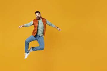 Full length young excited happy fun caucasian cheerful overjoyed man 20s years old wear orange vest mint sweatshirt jump high spreading outstretched hands isolated on yellow color background studio