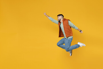 Full length side view of young powerful fun caucasian man 20s wearing orange vest mint sweatshirt jump high makes fly gesture isolated on yellow background studio portrait. Real heroes defend you