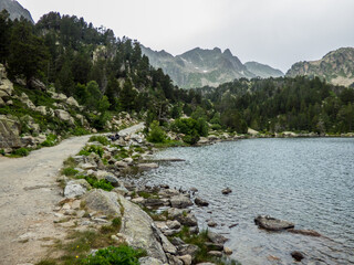 Un camino discurre a orillas de un lago de alta montaña rodeado de rocas y bosques de coníferas en el Parque Nacional de Aigües Tortes, en los Pirineos españoles