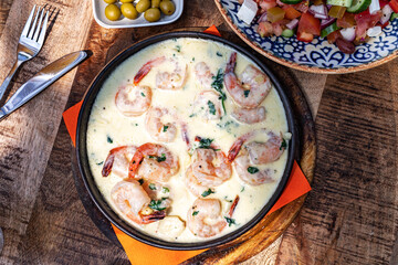 Shrimps in a creamy sauce in a frying pan on a wooden round board. Mediterranean Food, top view