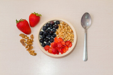 Healthy homemade breakfast. Yogurt with fresh fruits as strawberries, blueberries and nuts in a bowl with spoon on a wooden white table. Top view with selective focus.