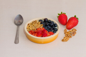 Bowl with natural yogurt and fresh fruits on wooden white table. Strawberries, blueberries and nuts with selective focus. Close up.