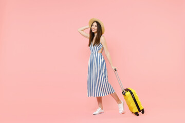 Full length traveler tourist woman in summer clothes hat hold yellow valise suitcase walk go isolated on pastel pink background. Passenger travel abroad weekends getaway Air flight journey concept