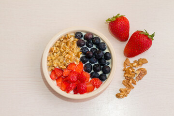 Healthy homemade breakfast. Yogurt with strawberries, blueberries and nuts in a bowl on a wooden white table. Top view.
