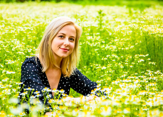 Naklejka na ściany i meble Blonde woman in black dress is sitting in countryside chamomiles flowers field