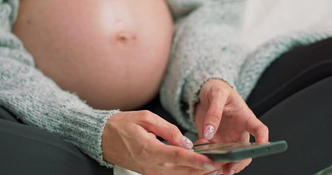 Close up of hands typing a text message on mobile phone. Young pregnant woman scrolling pictures phone. surfing internet